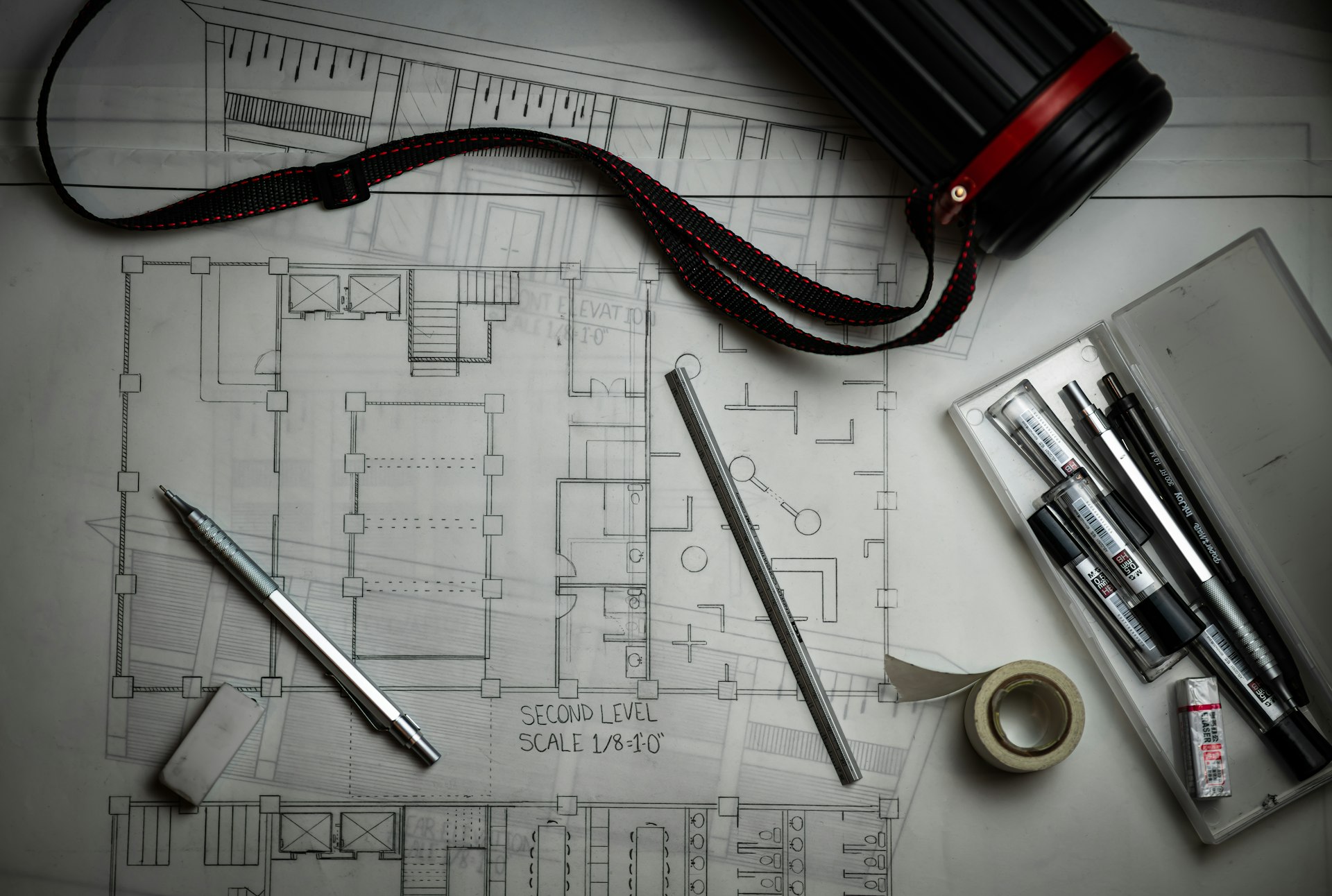 Architectural blueprints with drafting pencils, a metal ruler, and a storage tube